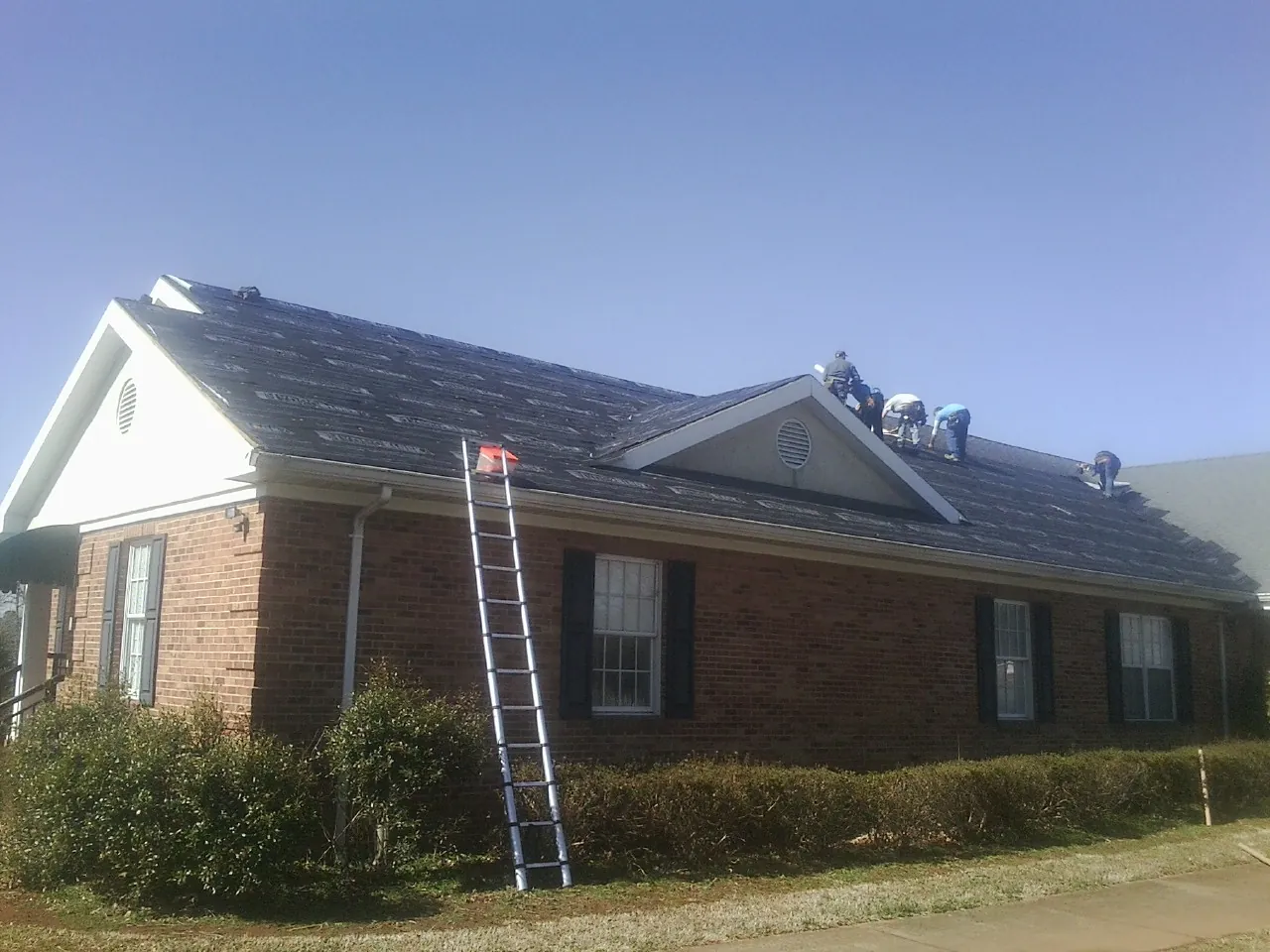 Crew tearing shingles off a brick ranch roof with a ladder set — Emergency Roof Repair work by our crew in Lemont Furnace