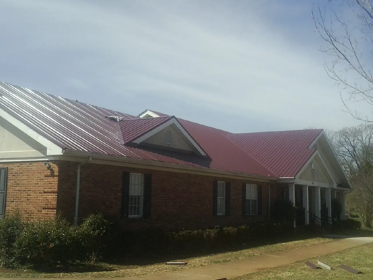 Red metal roof with gabled entries on a long brick building, from a Hail Damage Roof Repair job in Lemont Furnace