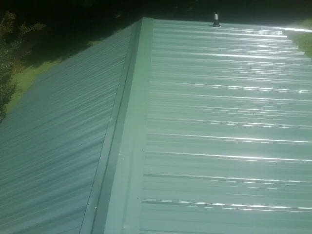 New green metal panels meeting at the ridge of a roof — Flat Roof Repair work by our crew in Lemont Furnace