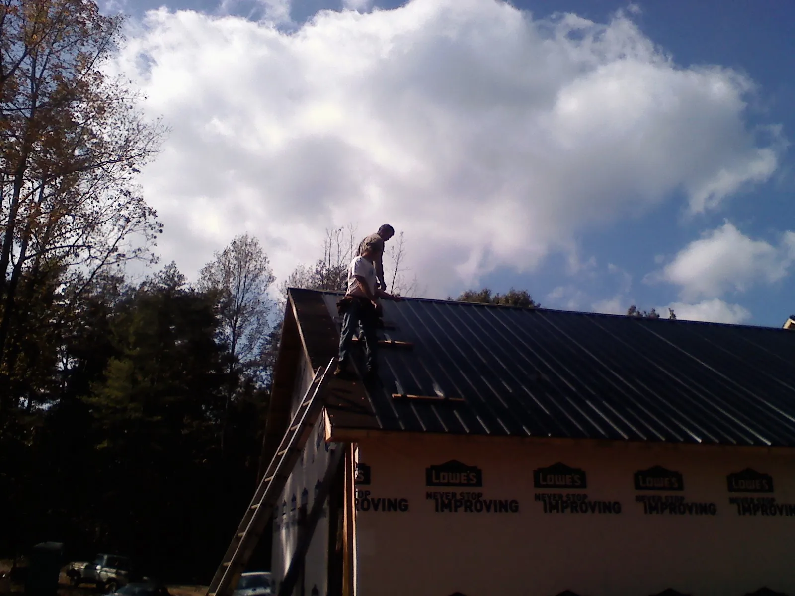 Roofer fastening dark metal panels high against a cloudy sky, from a Roof Inspection job in Lemont Furnace