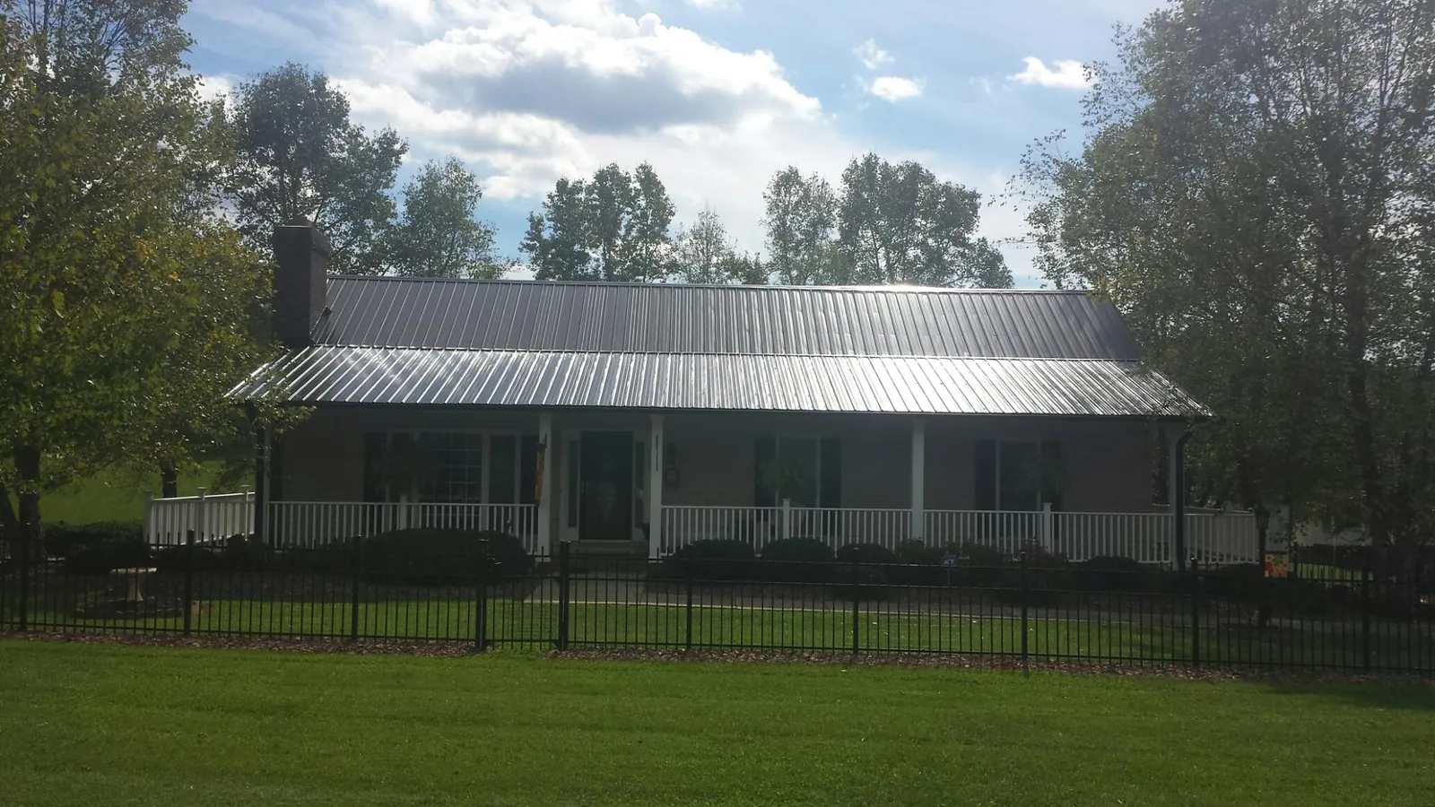Gray metal roof on a brick ranch with a full width front porch — Gutter Guard Installation work by our crew in Lemont Furnace