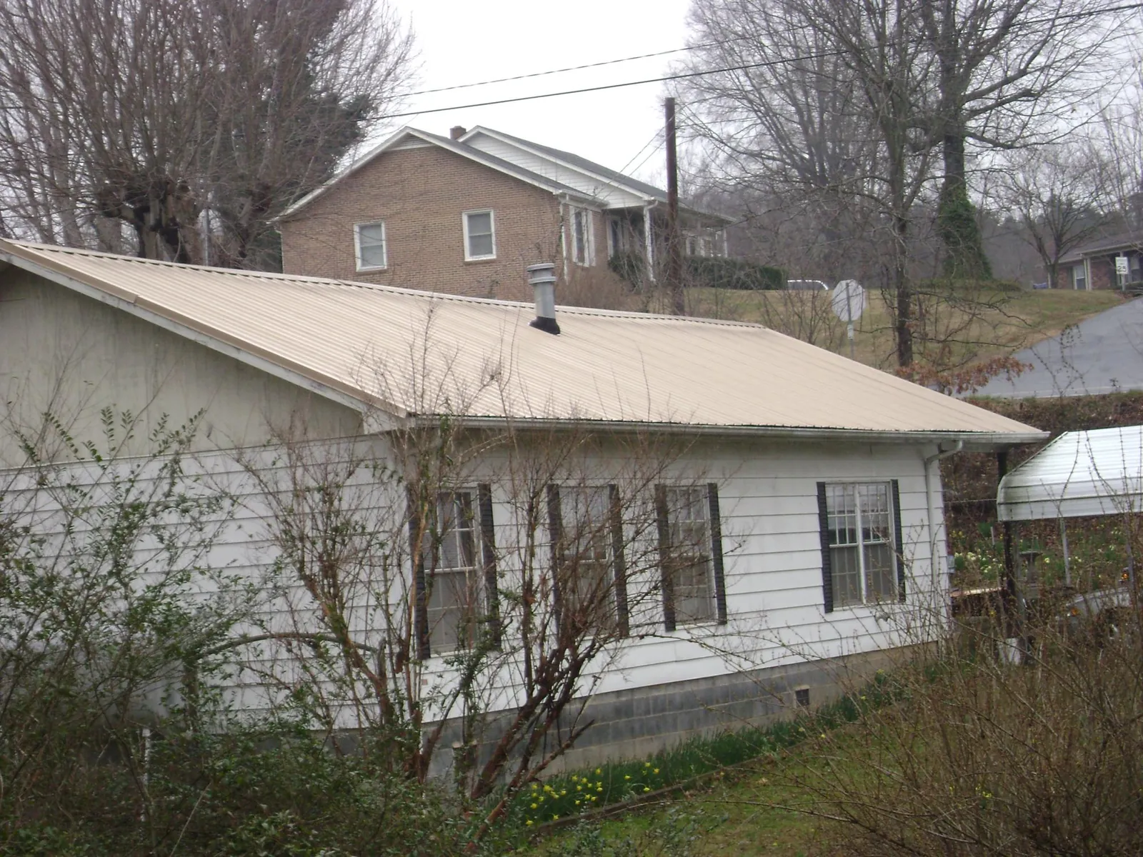 Tan metal roof on a white sided house set into a hillside — Commercial Roofing by Roofing Brothers in Lemont Furnace